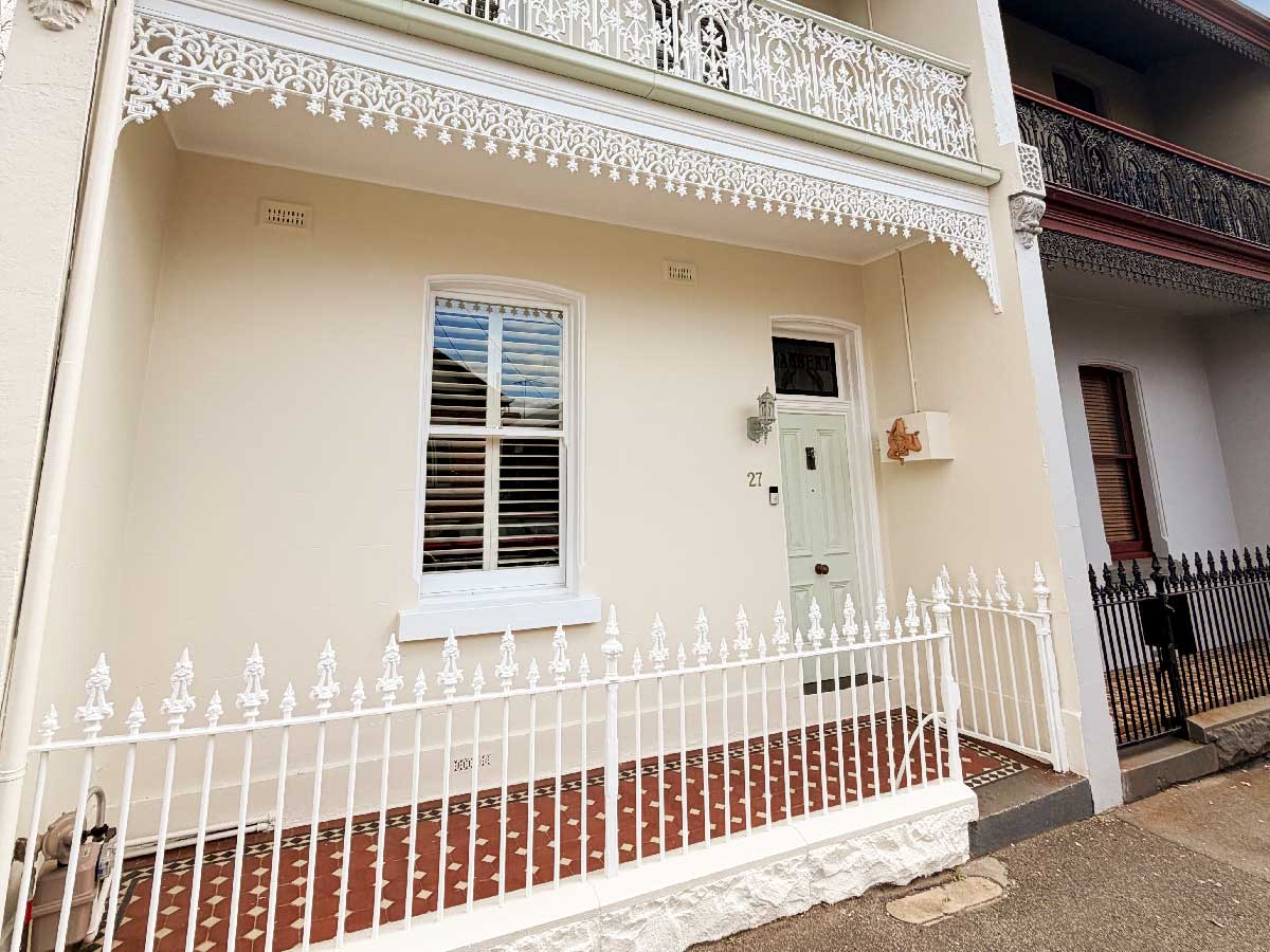 Freshly painted Victorian terrace with cast iron lacework, picket fence and tessellated tiles